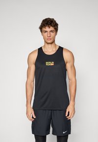 Schwarzes Sporttanktop mit einem strukturierten Muster, das ein lebhaftes "BERLIN RUN"-Logo in Gelb und einen kleinen Nike-Swoosh zeigt.