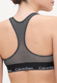 Svart-hvitt stripete sportsbh med racerback-design og bredt bånd med "Calvin Klein"-logo i kontrasterende hvit tekst.