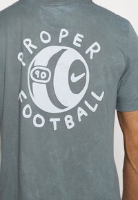 Camiseta de algodón gris con un gran gráfico blanco de un balón de fútbol y las palabras "PROPER FOOTBALL" impresas en letras negritas.