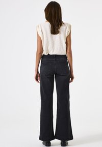 Jeans de pierna ancha negros con cintura alta, que cuentan con bolsillos traseros y un dobladillo limpio. Combinados con una blusa ligera de textura crema.