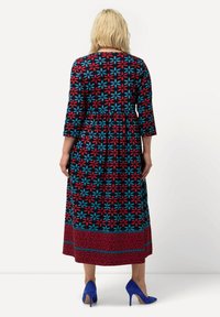 Abito maxi a stampa floreale in nero, con fiori rossi e blu, maniche 3/4, vita arricciata e orlo con motivo a contrasto rosso; abbinato a tacchi blu.