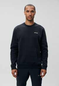 Sweatshirt noir à col rond en tissu doux, arborant un petit logo Columbia blanc sur la poitrine gauche et des poignets et un ourlet côtelés.