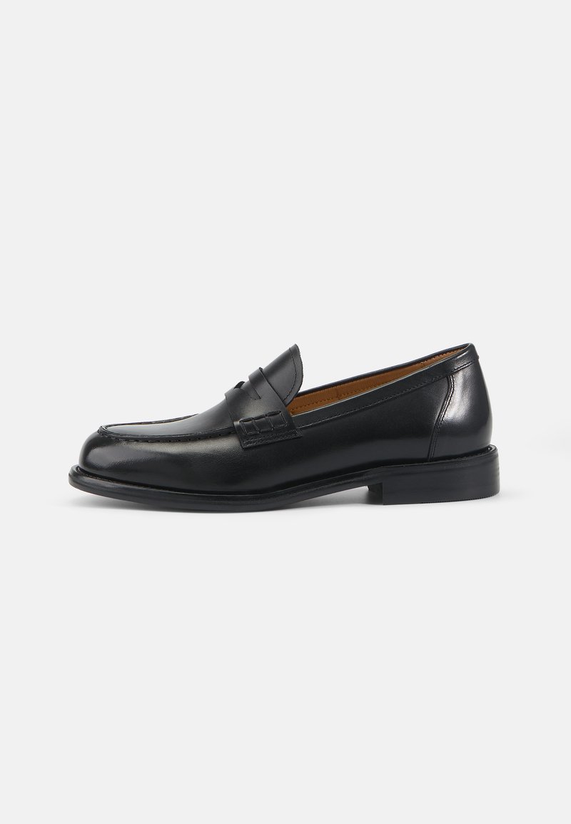 Mocassins en cuir noir avec une finition lisse, un talon bas, des détails cousus et une sangle décorative sur le devant. Design classique.