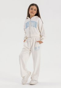 White zip-up hoodie with blue "BOSTON" text and matching sweatpants featuring "USA 1967" print; made of soft, smooth fabric.