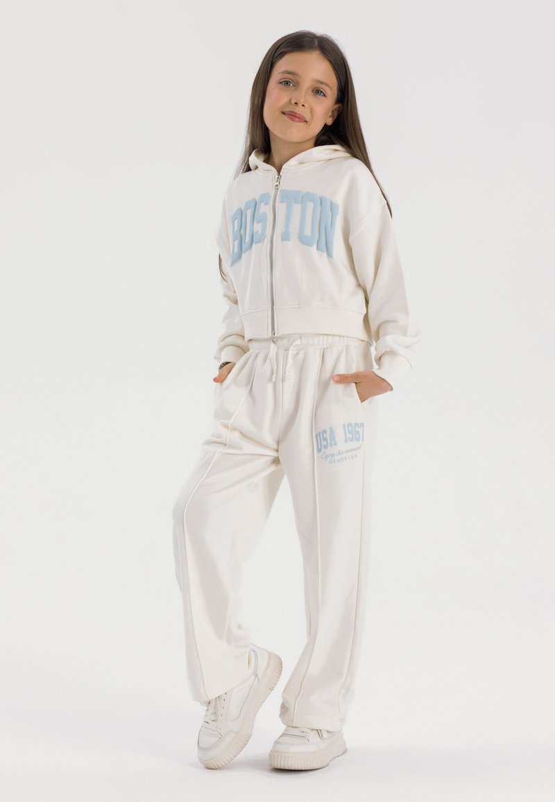 White zip-up hoodie with blue "BOSTON" text and matching sweatpants featuring "USA 1967" print; made of soft, smooth fabric.