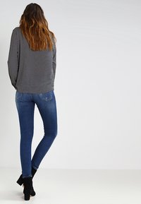 Haut à pois noirs et blancs à manches longues, associé à un jean bleu moulant et des bottines noires, vu de dos.