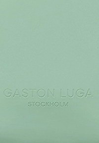 Ljust grön, texturerad bakgrund med upphöjd text: "GASTON LUGA STOCKHOLM" i mitten. Enkel, minimalistisk design.