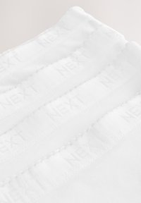 Baltas medvilninis audinys su tekstūruotomis juostelėmis, kuriose iškaltas žodis "NEXT", išdėstytas sluoksniais vienas ant kito. Siūlių detalės matomos palei kraštus.