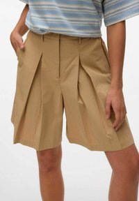 Beige geplooide shorts van lichtgewicht stof, met zakken, een tailleband en een relaxed fit. Gladde textuur met scherpe lijnen.