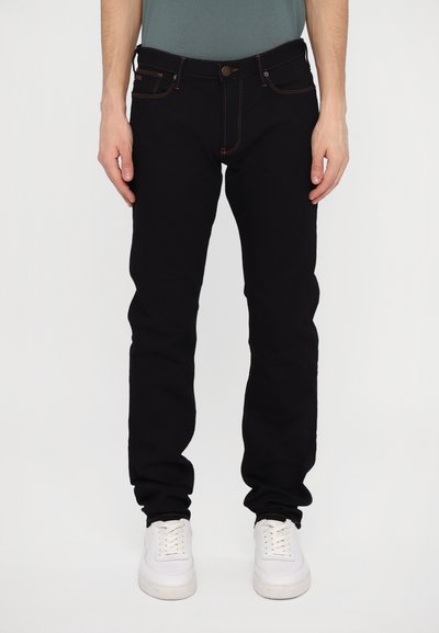 Jeans negri din denim cu o croială slim, cu cusături portocalii, cinci buzunare și închidere cu buton metalic. Asortați cu adidași albi.