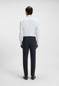 Vit skjorta med små blå prickar, kombinerad med mörkblå byxor. Rak skärning, långa ärmar och knäppning vid kragen.