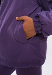 Paarse windbreakerjack met elastische manchetten en zijzak. De stof is soepel en lichtgewicht, ideaal voor buitenactiviteiten.