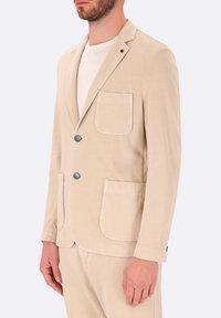 Blazer in cotone beige con due tasche frontali, chiusura a un bottone e rever a scollatura. Presenta una texture liscia e un delicato lucido.