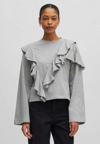 Grauer Langarm-Oberteil mit einem Rüschendesign auf der Vorderseite. Hergestellt aus einem weichen Stoff mit einem lockeren Schnitt und verkürzter Länge. Verfügt über weite Ärmel.