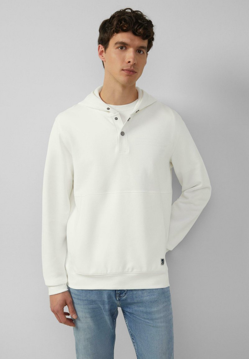 Witte pullover hoodie met een voorzak, trekkoord bij de hals en drukknopen. Zachte textuur, gecombineerd met lichtblauwe jeans.
