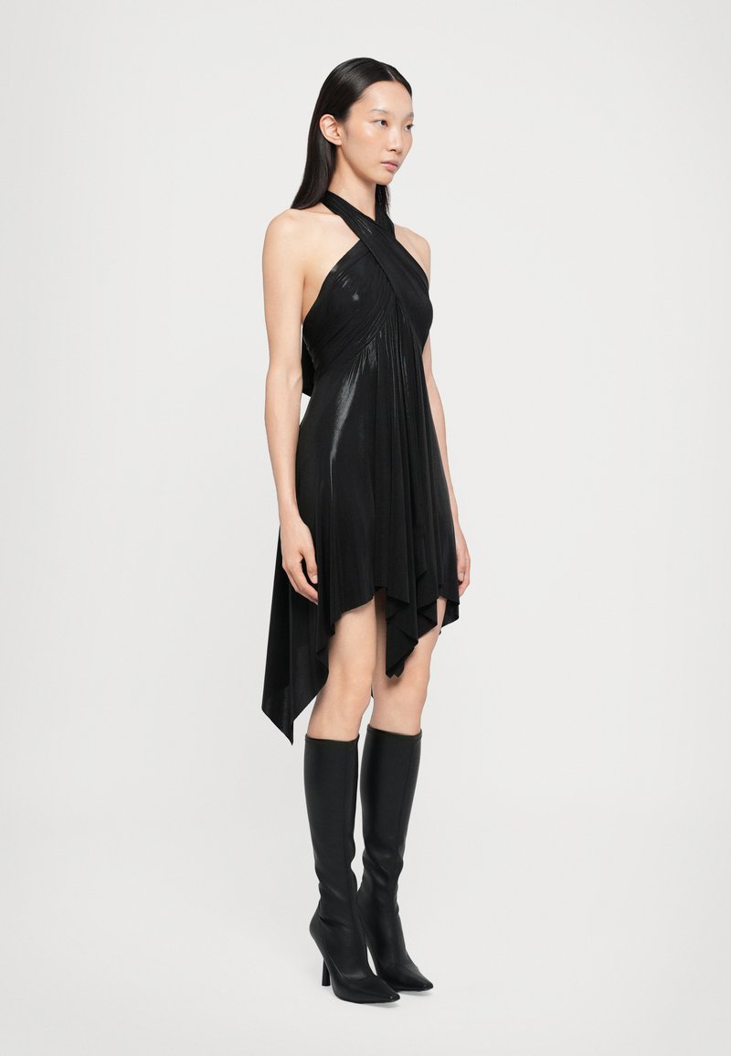 Vestido negro sin mangas con dobladillo asimétrico, tela drapeada y textura brillante. Combinado con botas de tacón negro lisas hasta la rodilla.