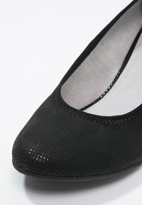 Chaussure ballerine noire pour femme avec dessus texturé et intérieur coussiné gris sur fond blanc.