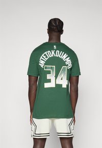 Žalias marškinėliai su užrašu "ANTETOKOUNMPO" ir numeriu "34" ant nugaros, turintys apvalų kaklą ir trumpas rankoves; dėvimi su baltais tinkliniais šortais.