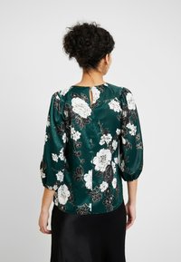 Floral blouse in dark green satin with black and white flower patterns, puffed sleeves, and a keyhole opening at the back.