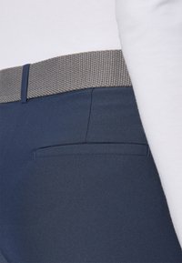 Pantaloni bleumarin cu un brâu texturat din tricot gri, având un buzunar lateral și o croială netedă, adaptată.