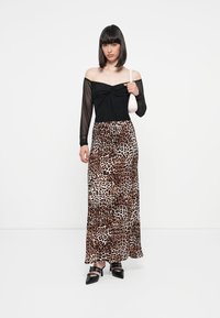 Top noir à épaules dénudées avec des manches longues transparentes, associé à une jupe maxi à imprimé léopard. Le mannequin porte un petit sac à main blanc et des talons noirs.