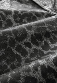 Tissu à imprimé animal noir présentant une surface texturée avec des nuances variées. Le motif a un éclat lisse et une profondeur subtile.