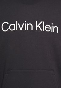 Black sweatshirt featuring a large white "Calvin Klein" logo on the front. Soft fabric with a kangaroo pocket at the bottom.