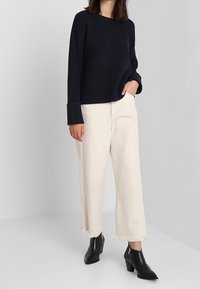 Navy žebrovaný pletený svetr, smetanové kalhoty širokého střihu s třásněmi na lemu a černé kotníkové boty s špičatou špičkou a zipovým detaily.