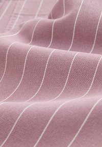Tissu rose pâle avec de fines rayures verticales blanches, montrant la texture et de légers plis sur la surface.