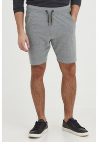 Pantalones cortos grises con cintura elástica y cordón, con bolsillos laterales y tejido texturizado. Combinados con zapatillas negras.