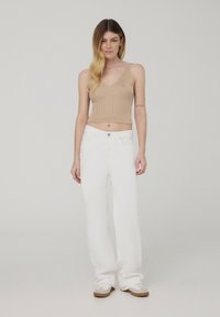 Top corto a coste beige con scollatura a V abbinato a pantaloni bianchi a gamba larga. Le scarpe sono basse, bianche con dettagli marrone chiaro.