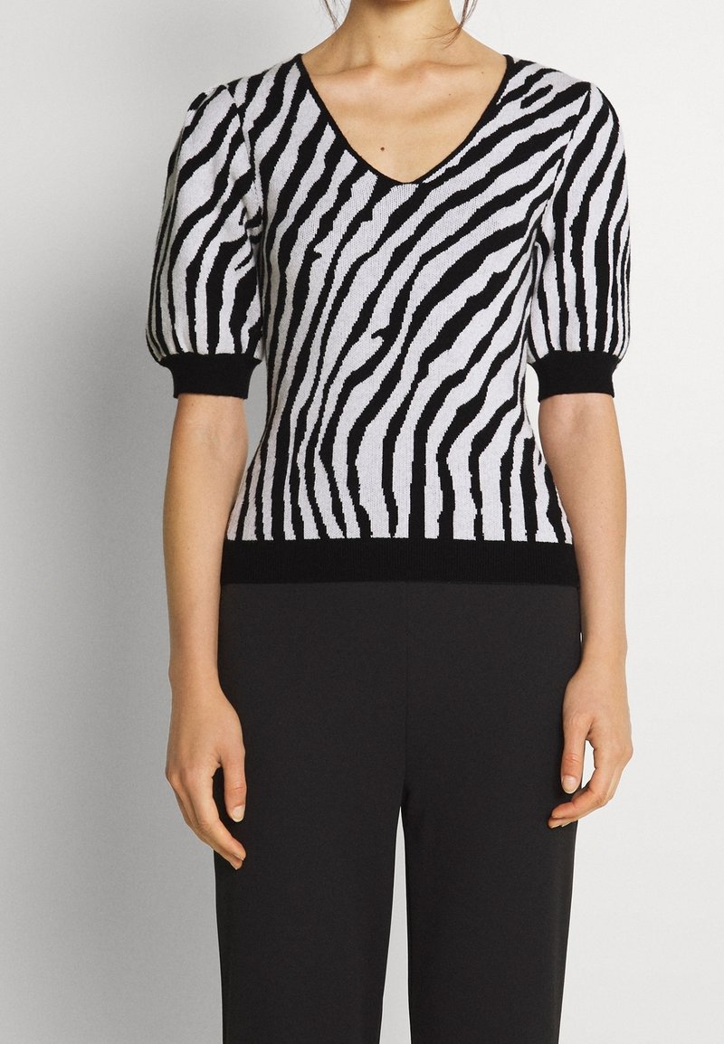 Top de punto a rayas blancas y negras con escote en V y mangas cortas abullonadas, con detalles acanalados negros en los puños y el dobladillo.