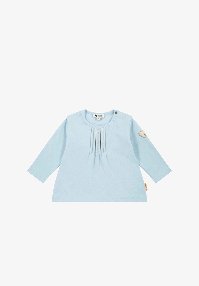 Světle modré dětské tričko s dlouhým rukávem, s nařasením v přední části, patentním knoflíkem na rameni a malou nášivkou medvídka na levém rukávu.