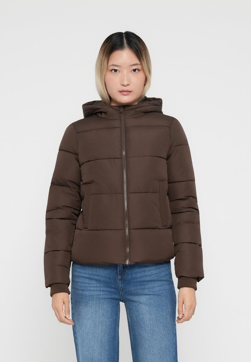 Veste rembourrée marron avec capuche, dotée de manches longues, d'un motif de matelassage horizontal, d'une fermeture éclair à l'avant et de deux poches. Portée avec un jean bleu.