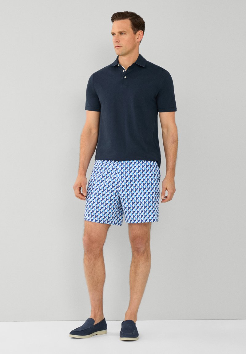 Polo shirt bleu marine, short de bain à motifs bleu et blanc, et chaussures slip-on bleu foncé. Tissu lisse avec une coupe classique.