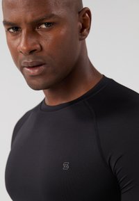 Black athletic short-sleeve shirt made from smooth, stretchy fabric. Features a subtle logo on the left chest and raglan sleeve design.