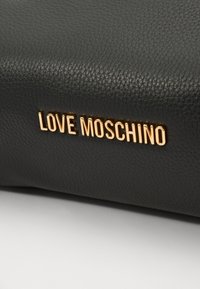 Bolso de cuero negro texturizado con una placa dorada de "LOVE MOSCHINO". La superficie tiene un acabado con textura de guijarro y un detalle sutil.