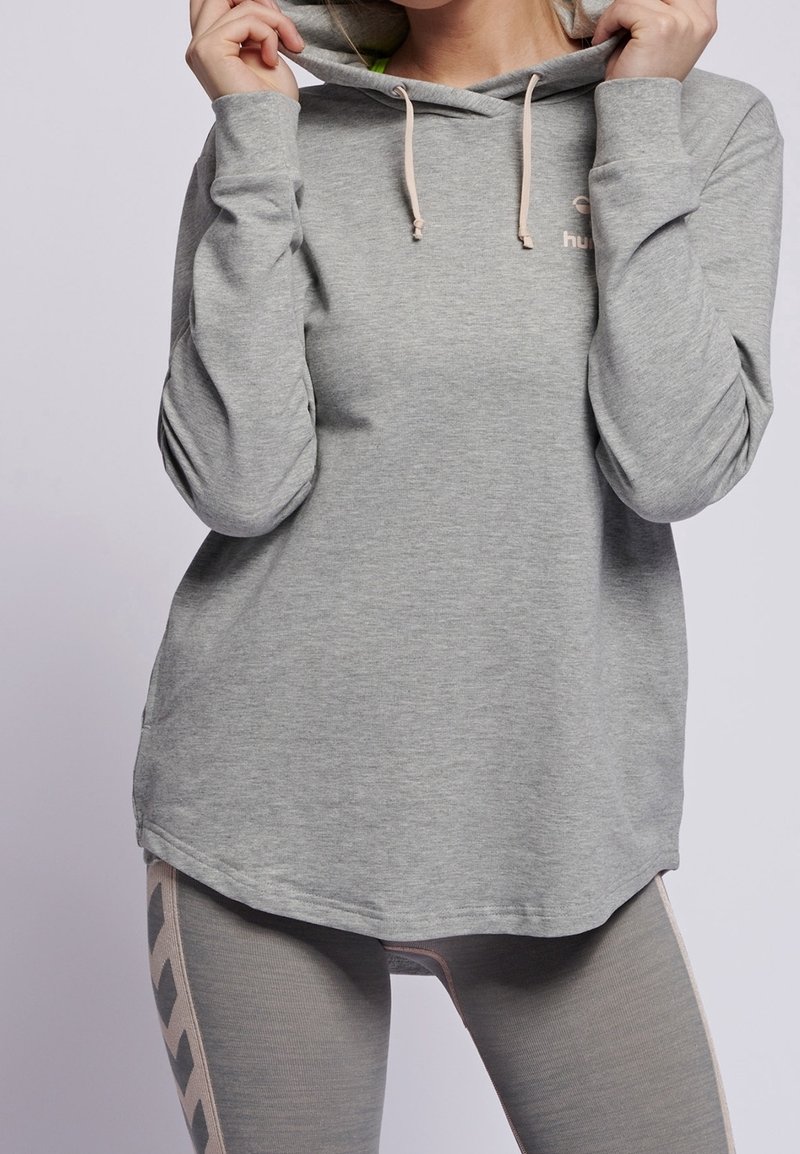 Hoodie gris clair en tissu doux avec une capuche à cordon de serrage, présentant un logo discret sur la poitrine et des manches longues.