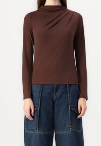 Brun långärmad topp med draperad halsringning och slät textur, i kombination med löst sittande mörkblå vida cargobyxor med fickor.