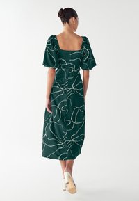 Groene jurk met een vierkante halslijn, pofmouwen en een getailleerde taille, met een wit abstract lijnenpatroon en een lengte tot onder de knie.