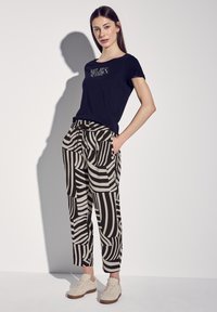 T-shirt noir avec du texte, associé à un pantalon à motifs avec des rayures alternées noires et beiges. Baskets beiges à lacets.