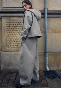 Hanorac scurt gri cu glugă ajustabilă și croială supradimensionată, asortat cu pantaloni gri largi. Material moale, texturat, cu buzunare pe pantaloni.