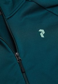 Petrolejová bunda so zipsom vyrobená z hladkej látky. Má výrazné logo vo svetlozelenej farbe a čierny zips. Viditeľný je textúrovaný povrch.