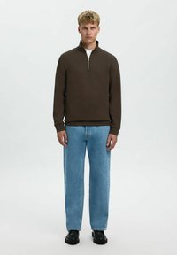 Hnědý svetr s vysokým límcem a detailem na půl zip, kombinovaný se světle modr ými širokými džíny a černými chunky botami. Jednoduchý design a textury.