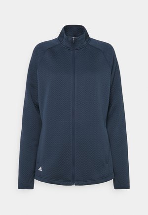 Veste bleu marine zippée intégralement avec tissu texturé en chevron, manches longues, col montant et petit logo Adidas près de l'ourlet inférieur.