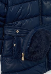 Chaqueta acolchada de color azul marino con bolsillos de botones a presión, cremallera dorada y pouch de llavero de pelo sintético azul marino.