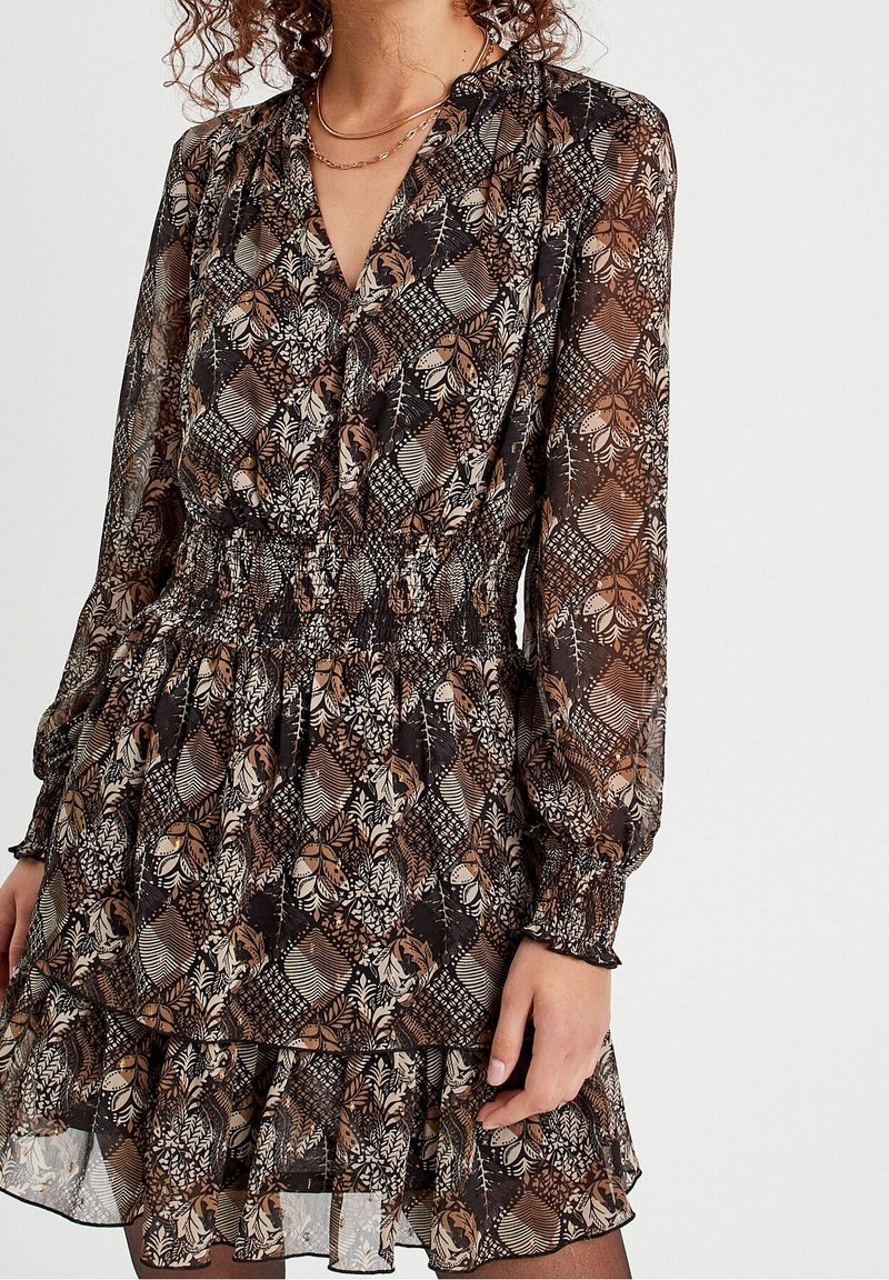 Robe courte à motifs avec des manches longues, une taille smockée et un ourlet volé. Présente des motifs floraux et géométriques en marron foncé, crème et or.