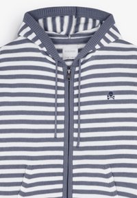 Gestreepte grijze en witte zip-up hoodie met een gebreide textuur, een capuchon, zijzakken en een klein doodskoplogo op de borst.