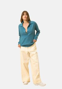 Turkos ulltröja med bred krage, kombinerad med krämfärgade, vida byxor. Outfitten har en avslappnad passform och mjuk textur.