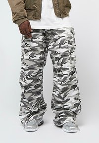 Kargo kalhoty v šedém maskáčovém vzoru s několika kapsami. Vyrobeny z lehké tkaniny, mají uvolněný střih a elastické manžety.